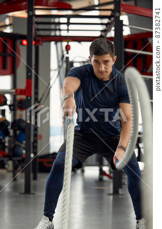 Man holding a pair of battle ropes for workout. guy at the gym working out with fitness rope. 87382741
