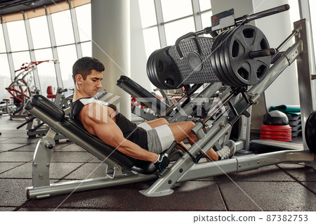Training legs in the simulator, the athlete works with his legs on the simulator, working out the muscles on the legs Training legs in the simulator, the athlete works with his legs on the simulator, working out the muscles on the legs 87382753
