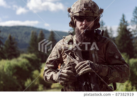 War concept. A bearded soldier in a special forces uniform fighting an enemy in a forest area. Selective focus  87382919
