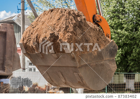 Excavation works. Tractor bucket digging the ground on a construction site against the sky Excavation works. Tractor bucket digging the ground on a construction site against the sky 87383402