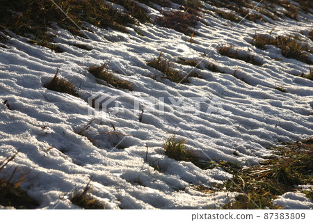 The snow on the side of the embankment melts and becomes uneven and continuous 87383809