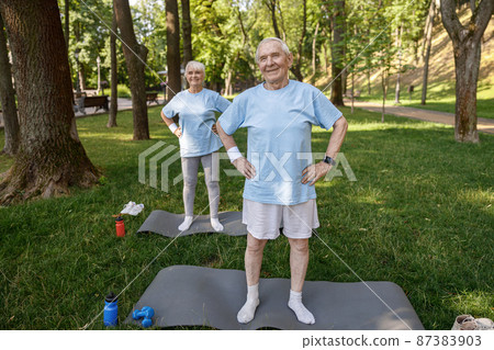 Sportive mature man and woman train on mats on lush lawn Sportive mature man and woman train on mats on lush lawn 87383903