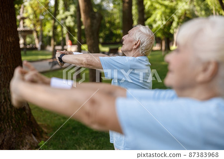 Grey haired mature man trains with woman on meadow in city park 87383968