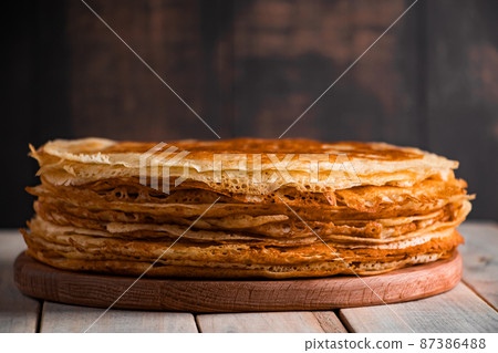 Traditional Russian food - thin pancakes. A stack of crepes on a dark brown wooden background. Rustic style. Traditional Russian food - thin pancakes. A stack of crepes on a dark brown wooden background. Rustic style. 87386488