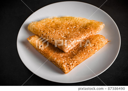 Thin pancakes on a plate on a black background, traditional Russian food. 87386490