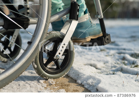 Close-up of legs of woman in wheelchair in winter outdoors. Close-up of legs of woman in wheelchair in winter outdoors. 87386976
