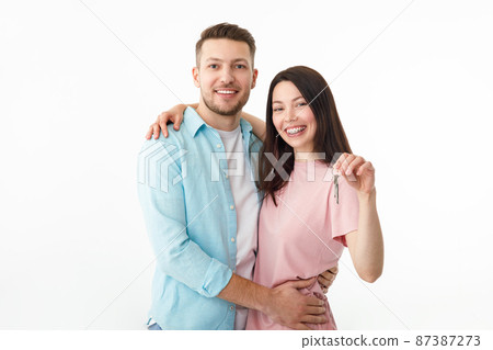 A cheerful young couple is hugging in the kitchen, holding the keys to a new house in their hands. Happy newlyweds moved into a new apartment, got a mortgage, moving day. 87387273