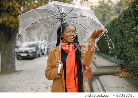 Young black woman in a coat standing under a transparent umbrella outside 87388783