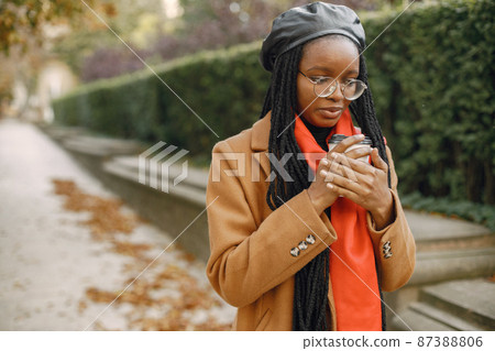 Young black woman in a coat drinking coffee outside Young black woman in a coat drinking coffee outside 87388806