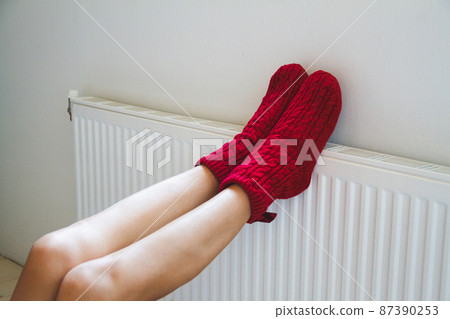 A young woman in warm, cozy knitted socks warms her legs by the 87390253