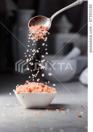 Pink salt in crystals is poured into a small white bowl. Pink salt in crystals is poured into a small white bowl. 87393580