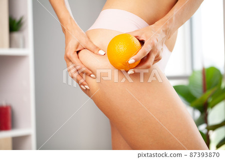Cellulite problem, young woman holding orange near her leg 87393870