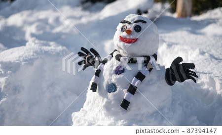 Snowman in a striped scarf. Christmas decorations made of snow. 87394147