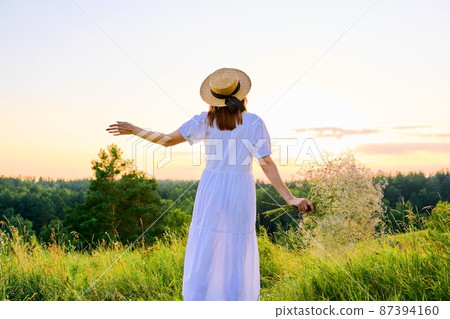 Back view of romantic woman in a white dress with a straw hat enjoying sunset Back view of romantic woman in a white dress with a straw hat enjoying sunset 87394160