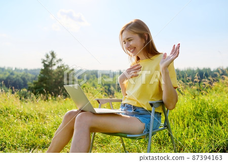 Summer vacation in wild meadow, adult woman resting on folding chair for camping using laptop Summer vacation in wild meadow, adult woman resting on folding chair for camping using laptop 87394163