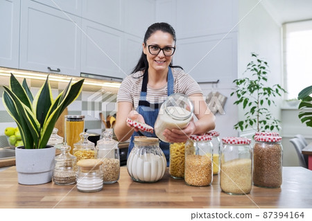 Smiling woman in the kitchen with jars of stored food. Smiling woman in the kitchen with jars of stored food. 87394164