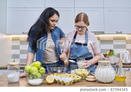 Mother and teenage daughter cooking at home in the kitchen. Mother and teenage daughter cooking at home in the kitchen. 87394165