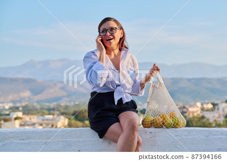 Happy middle aged woman talking on mobile phone outdoor. Happy middle aged woman talking on mobile phone outdoor. 87394166