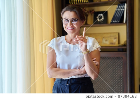 Portrait of confident successful middle aged woman looking at camera, pointing finger gesture attention 87394168