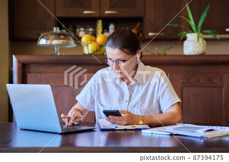 Home workplace, middle aged woman in headphones working using laptop 87394175