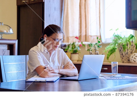 Serious mature woman in headphones talking on video using laptop Serious mature woman in headphones talking on video using laptop 87394176