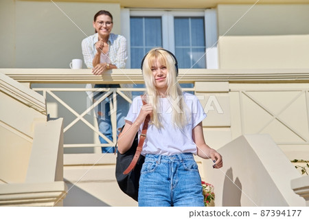 Middle-aged mother seeing off her teenage daughter on the porch of the house Middle-aged mother seeing off her teenage daughter on the porch of the house 87394177