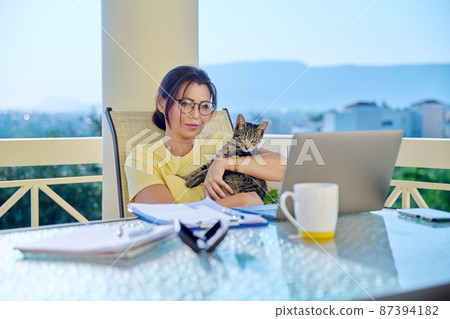 Middle-aged woman working at home with a cat in her arms. 87394182
