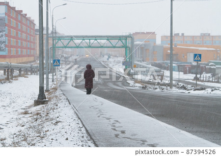Snowy weather in the city. A woman walks along the snow-covered sidewalk. 87394526