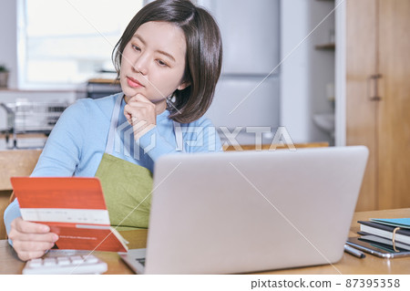 A young woman in an apron looking at her bankbook and thinking about her old age 87395358