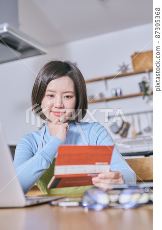 A young woman in an apron looking at her bankbook with a smile A young woman in an apron looking at her bankbook with a smile 87395368