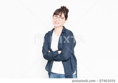Woman wearing glasses standing in front of a white background with her arms folded Woman wearing glasses standing in front of a white background with her arms folded 87401059