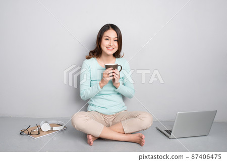 Happy casual beautiful asian woman working on a laptop sitting on floor at home. Happy casual beautiful asian woman working on a laptop sitting on floor at home. 87406475