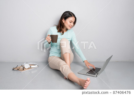 Happy casual beautiful asian woman working on a laptop sitting on floor at home. Happy casual beautiful asian woman working on a laptop sitting on floor at home. 87406476