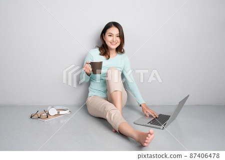 Happy casual beautiful asian woman working on a laptop sitting on floor at home. 87406478