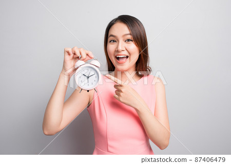 Pretty asian girl with surprised face holding an alarm clock in her hand and looking at it with opened mouth 87406479