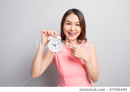 Pretty asian girl with surprised face holding an alarm clock in her hand and looking at it with opened mouth 87406480