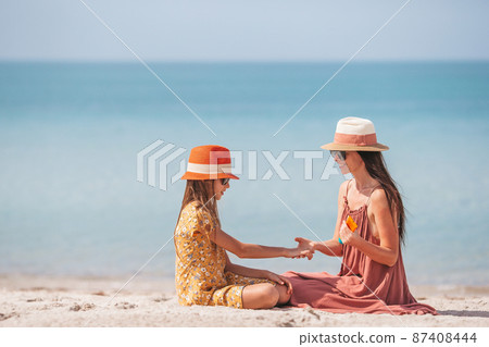 Young mother applying sun cream to daughter nose on the beach. Sun protection 87408444