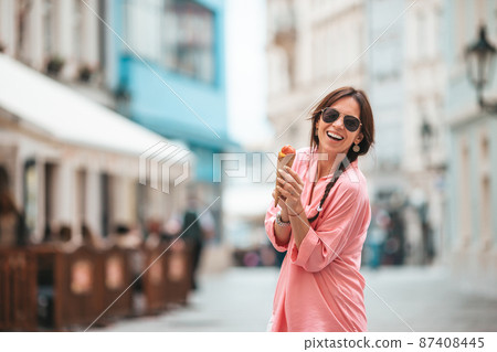 Happy young woman eating ice-cream on the street of european city. Happy young woman eating ice-cream on the street of european city. 87408445