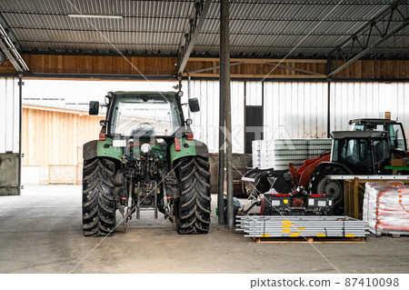 Green tractor with big wheels in garage near agricultural fixtures at daytime Green tractor with big wheels in garage near agricultural fixtures at daytime 87410098