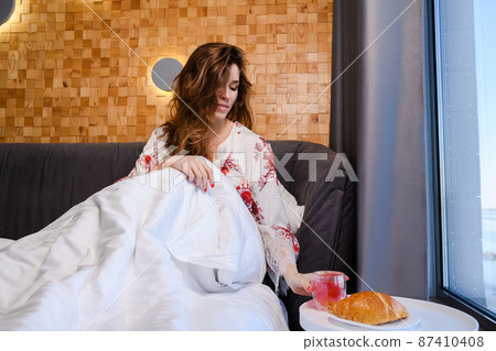Attractive young woman having breakfast in bed in the morning 87410408