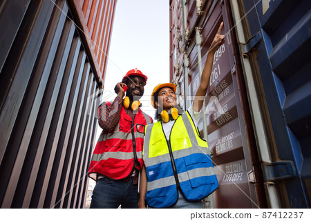 Two African american male and female worker using radio communication and checking control loading freight containers from Cargo freight ship for import export. Two African american male and female worker using radio communication and checking control loading freight containers from Cargo freight ship for import export. 87412237