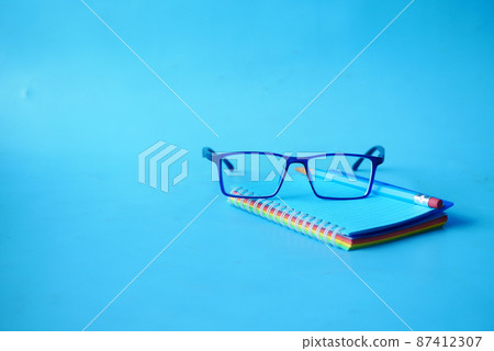 notepad, eyeglass and a pencil on blue color background notepad, eyeglass and a pencil on blue color background 87412307