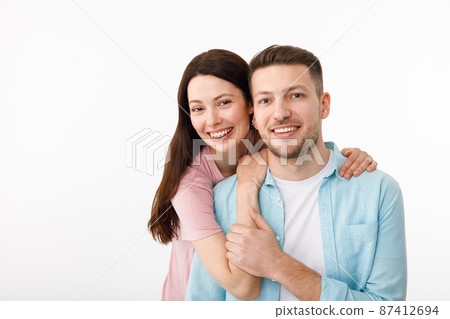 Portrait of a beautiful beloved couple. A guy and a girl hug each other and look at the camera smiling . On a white background Portrait of a beautiful beloved couple. A guy and a girl hug each other and look at the camera smiling . On a white background 87412694