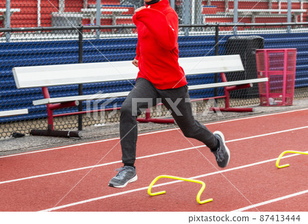 High school boy running over yellow mini hurdles on a track 87413444