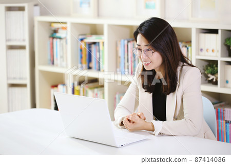 Office worker woman working from home via internet online with laptop smiling brightly Office worker woman working from home via internet online with laptop smiling brightly 87414086