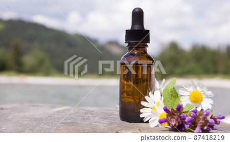 Composition with chamomile flowers and cosmetic bottle of essential oil. 87418219