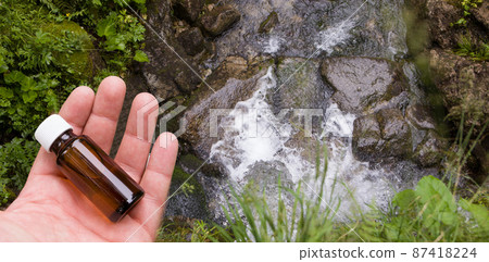 Medicine bottle on the water source background. A glass bottle with herbal extract in your hand. Medicine bottle on the water source background. A glass bottle with herbal extract in your hand. 87418224