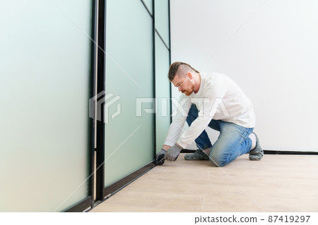 master adjusts sliding doors of wardrobe made of metal and glass. 87419297
