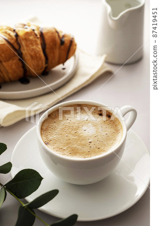 Coffee cup with fluffy milk foam and croissantson bright background. Breakfast time 87419451