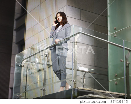 asian business executive talking on cellphone on top of stairs asian business executive talking on cellphone on top of stairs 87419545